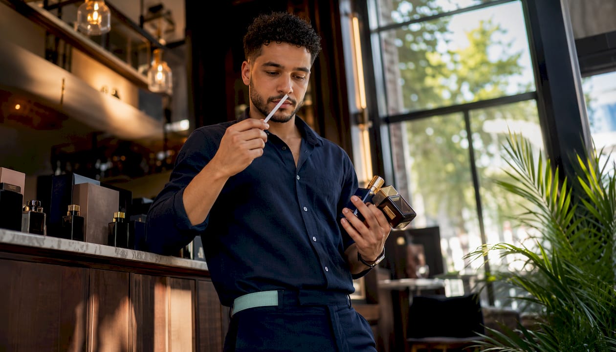 Man smelling cologne tester in bedroom