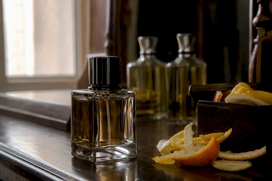 Primer plano de elegantes botellas de perfume y cáscaras de cítricos sobre el tocador