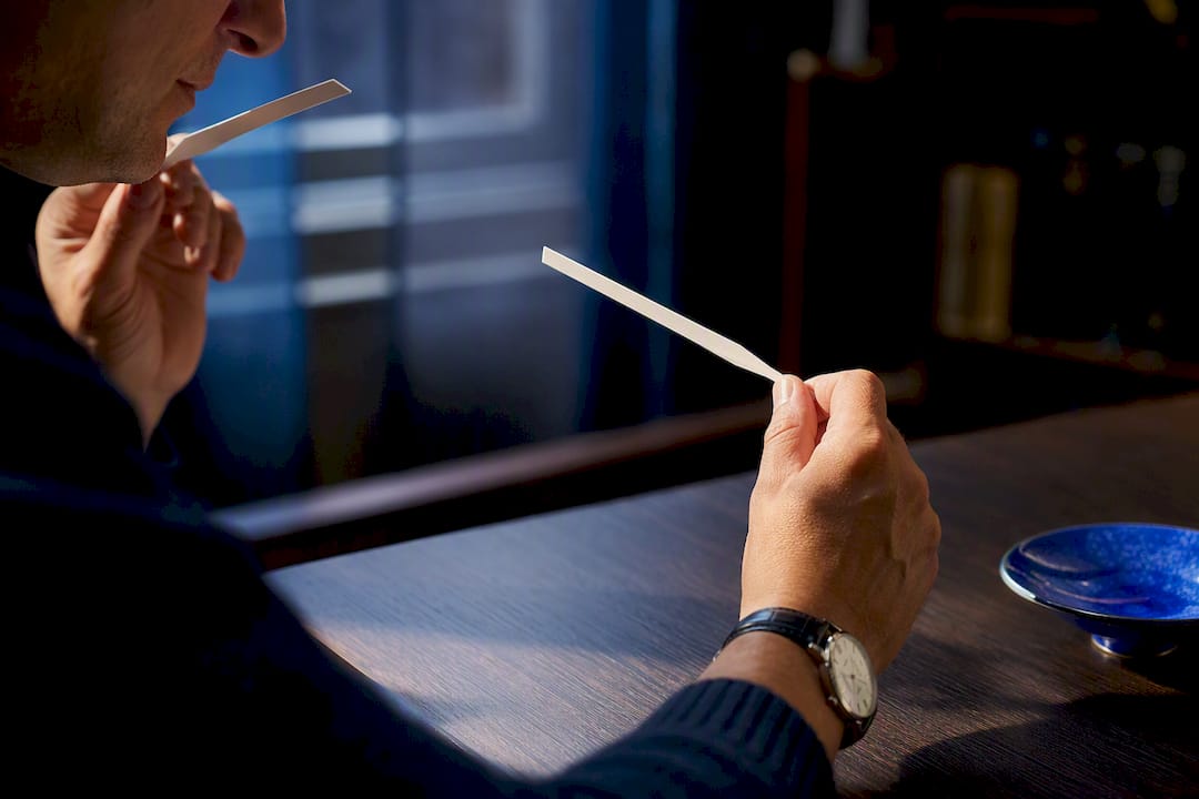 Hands evaluating two fragrance blotter strips