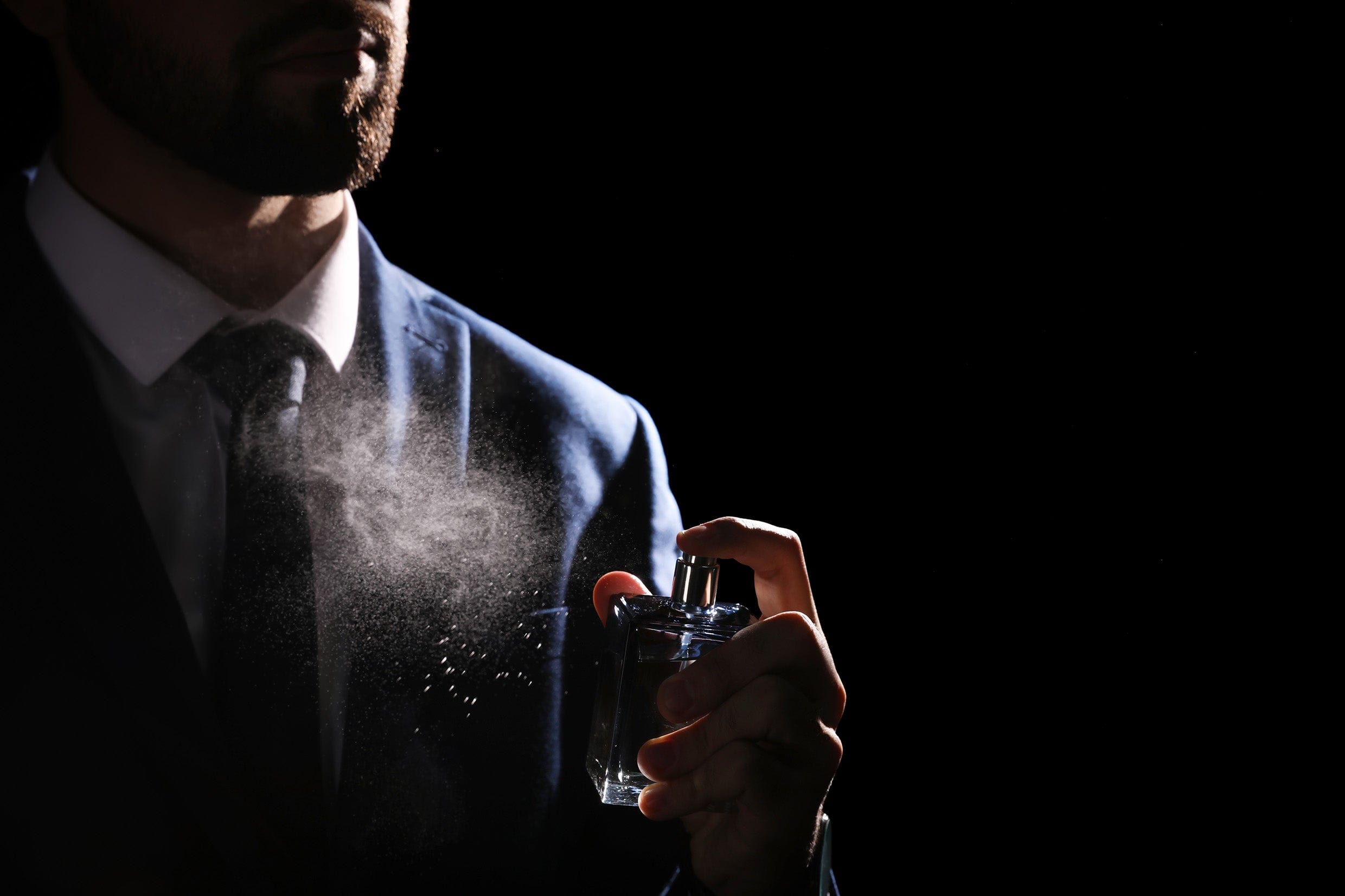 Man in a suit spraying perfume against a dark background